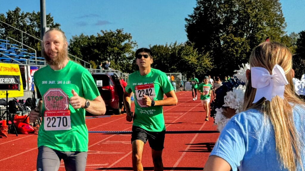 Two men running on a track. Brian Rock, on the left, was starting the 14th Annual Stop for Nikhil 5k race.